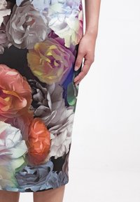 Main reposant contre une jupe à motif floral coloré avec de grandes roses sur fond noir.