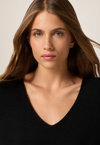 Zwarte V-hals top, zachte stof, aansluitend ontwerp, gladde textuur, met een natuurlijke V-vormige halslijn en een minimalistische esthetiek.