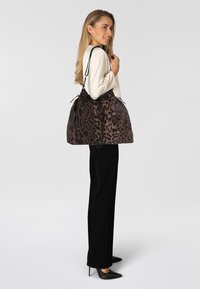 Bolso de mano con estampado de leopardo, fabricado en un tejido suave, en tonos marrón y negro, con cierre de cordón y asas negras. Diseño estructurado y espacioso.