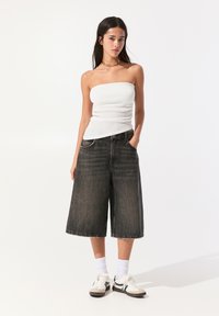 Culottes en denim noir à larges jambes, associés à un top sans manches à côtes blanc. Des baskets et des chaussettes blanches à la cheville complètent le look.