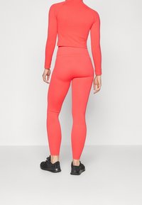 Completo da attivi color corallo composto da una maglia a maniche lunghe e leggings. Tessuto morbido e elastico; design aderente; abbinato a scarpe da corsa nere.