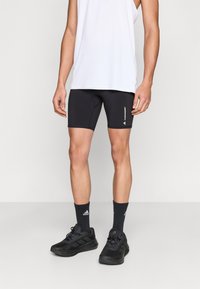 Μαύρο αθλητικό σορτς με εφαρμοστή γραμμή, συνδυασμένο με λευκό τοπ, μαύρα αθλητικά παπούτσια και μαύρες κάλτσες.