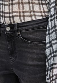 Κοντινό πλάνο μαύρου τζιν με ένα διάφανο, τσαλακωμένο πουκάμισο καρό σε ουδέτερους τόνους.