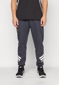 Gray sweatpants with white diagonal stripes on the lower legs, featuring a logo patch and ribbed cuffs. Paired with black athletic shoes.