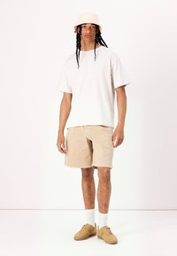 Witte short-sleeve T-shirt, beige shorts, beige bucket hat, tan sneakers en witte crew socks; relaxte pasvorm, eenvoudig ontwerp en zachte textuur.