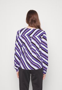 Long-sleeve blouse in lightweight fabric featuring diagonal stripes in purple, white, and black. Includes a back pocket and rounded hem.