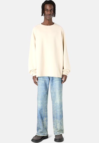 Beige oversized Sweatshirt mit langen Ärmeln, kombiniert mit hellblauen, ausgewaschenen, geraden Jeans und grauem Schuhwerk.