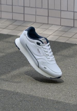 Baskets blanches avec une tige en cuir texturé, accents bleu marine, bout arrondi et semelle blanche rembourrée. Présente des lacets et un logo sur la languette.