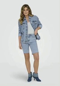 Gai zila denima jaka un šorti, apvienoti ar pelēku topu bez piedurknēm un ziliem potīšu zābakiem. Šortiem ir plīsums apakšmalā; jakai ir pogas.