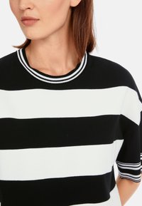 Black and white striped knit top with a round neckline, featuring a ribbed collar and short sleeves with accent stripes.