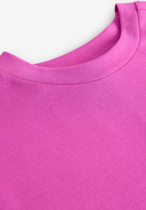 Vaaleanpunainen puuvillapaita, jossa on pyöreä pääntie ja lyhyet hihat. Paita on sileä ilman näkyviä kuvioita tai yksityiskohtia.