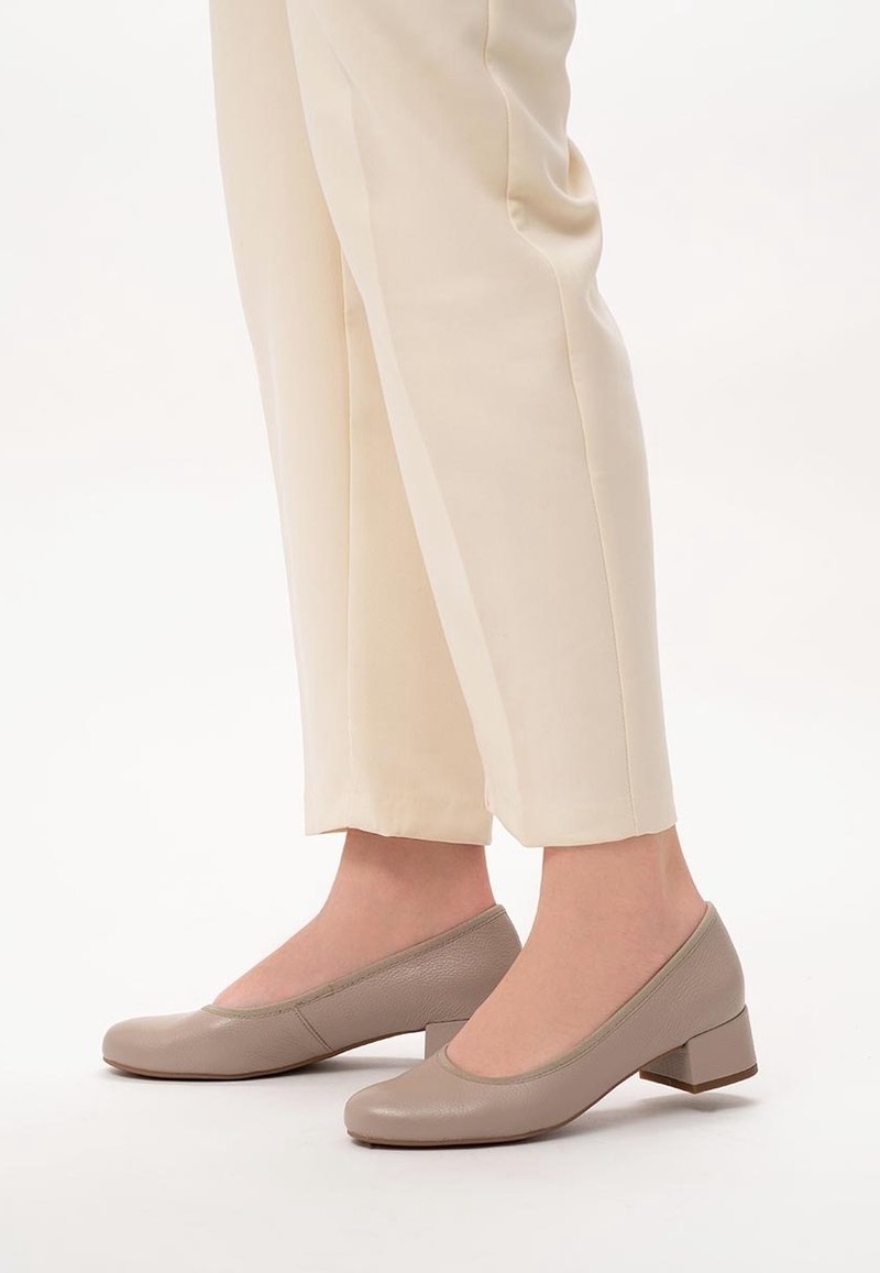 Chaussures en cuir beige à talon bloc avec un bout rond. Texture lisse et design minimaliste, associées à un pantalon de couleur crème.