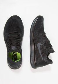 Chaussures de course en maille noire avec une tige texturée, des semelles intérieures vert néon contrastantes et une semelle en caoutchouc noire lisse. Elles arborent un logo Nike.