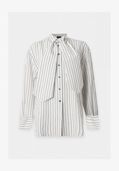 Blouse blanche à manches longues boutonnée avec fines rayures verticales noires et un grand détail de cravate asymétrique sur fond uni.