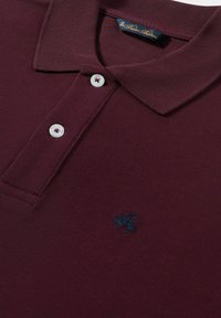 Burgundská polo košile vyrobená z texturované látky s límečkem, třemi bílými knoflíky a vyšitým modrým logem na levé hrudi.