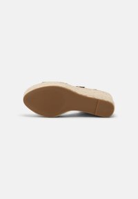 Sandale compensée avec semelle en caoutchouc texturée et talon plateforme enveloppé de jute, vue du dessous sur fond blanc.