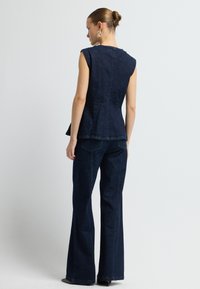 Námořnická denimová bezrukávová košile s rozšířeným lemem, ve spojení s odpovídajícími širokými kalhotami se zadními kapsami a texturovaným povrchem.