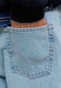 Lichtblauwe denim jeans met een achterzak met gebogen stiksels. De stof heeft een zachte textuur en een vervaagde afwerking.