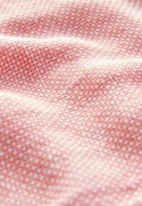 Tissu doux avec un motif texturé de petits fils blancs et roses entrecroisés créant un design tissé en forme de grille.
