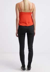 Top sin mangas rojo con tirantes finos, combinado con jeans negros ajustados. La tela es suave y los jeans tienen un diseño clásico de cinco bolsillos.
