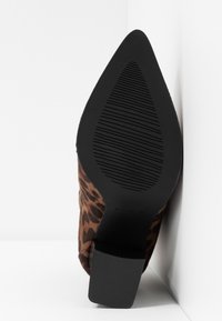 Chaussure à bout pointu imprimé léopard marron avec semelle noire texturée et talon bloc, photographiée par dessous sur fond blanc.