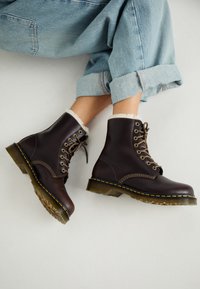Bottes de cheville en cuir marron avec un design à lacets, doublure en fourrure, couture jaune et semelles en caoutchouc épaisses. Portées avec un jean bleu clair retroussé.