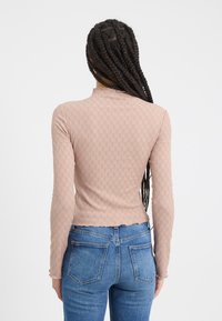 Langärmliges, hellrosa Oberteil mit strukturiertem Muster und gewelltem Saum, kombiniert mit blauen Jeans, die ein klassisches Taschendesign aufweisen.