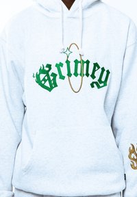 Sudadera gris con el texto bordado en verde y dorado "Grimey", con un diseño de llama en la manga izquierda y un bolsillo frontal.