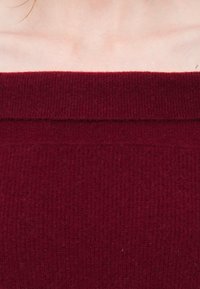 Μπορντό πλεκτό μπλουζάκι με ραμμένο σχέδιο και φαρδιά, εκτός ώμου λαιμόκοψη; ομαλή μετάβαση υφάσματος από το πάνω μέρος στο σώμα.