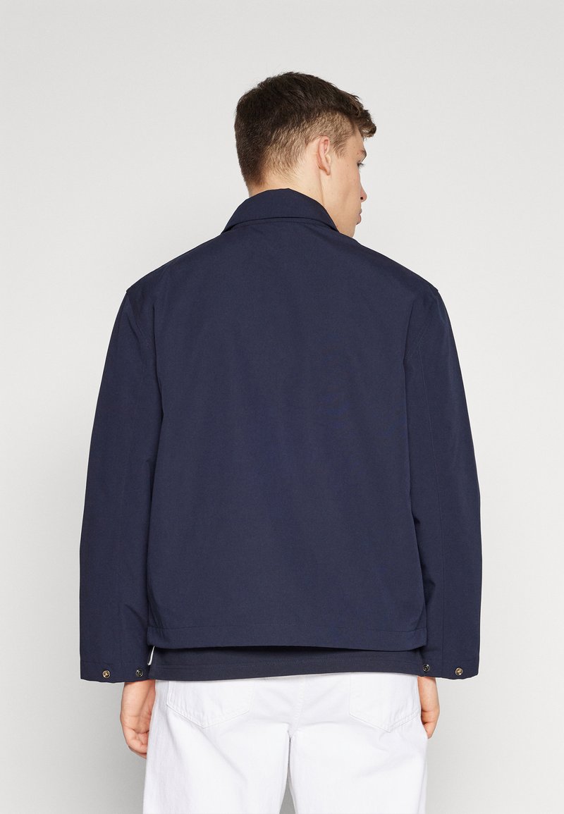 Giacca blu navy con vestibilità rilassata, colletto a punta e polsini con bottoni. Vista posteriore che mostra un tessuto morbido e una lunghezza leggermente accorciata.