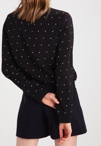 Maglietta nera a maniche lunghe con pois bianchi, caratterizzata da una texture liscia e un design aderente, abbinata a pantaloni corti blu navy.