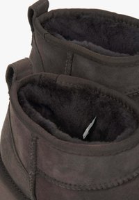 Bruine suède enkellaarsjes met een zachte, donkere bontvoering, voorzien van een gestikte naad en stoffen lussen bij de opening.