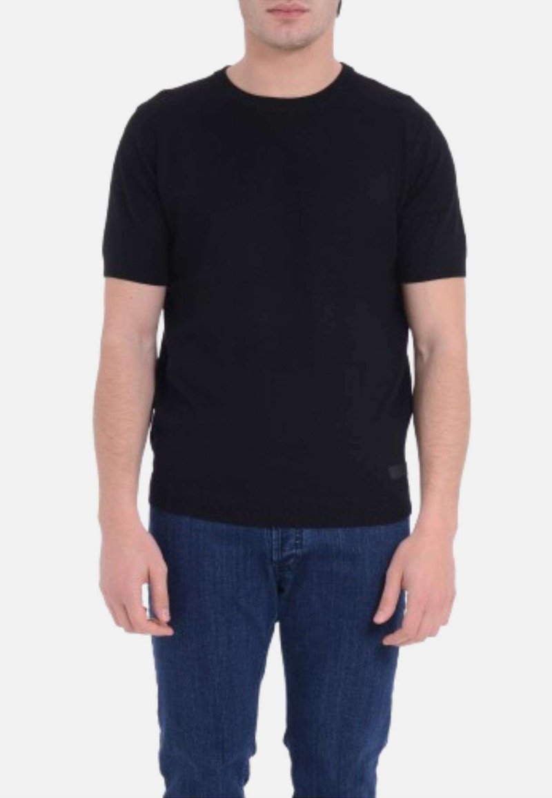 T-shirt nera a maniche corte realizzata in un tessuto morbido, con scollatura rotonda e taglio aderente. Abbinata a pantaloni in denim blu.