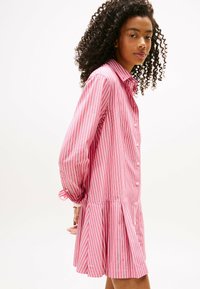 Sukienka w paski w kolorze różowym i białym, zapinana na guziki, z długimi rękawami zakończonymi guziczkami, rozkloszowanym dołem i lekką tkaniną.