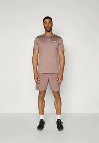 Camiseta atlética de manga corta en marrón claro, combinada con pantalones cortos a juego. Presenta un logotipo sutil, tejido transpirable y un corte relajado.