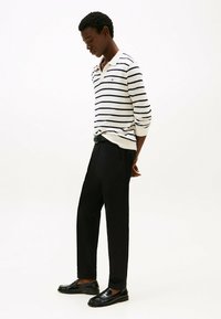 Polo a maniche lunghe a righe in crema e blu navy, abbinato a pantaloni neri e mocassini. Il polo ha un colletto e un piccolo logo.
