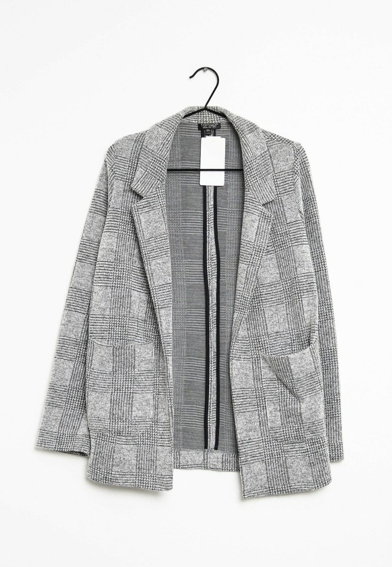Blazer à carreaux gris et blanc avec revers et deux poches avant, suspendu sur un cintre noir sur fond blanc.