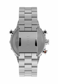 Montre en acier inoxydable avec un bracelet à maillons argentés. Boîtier rond avec boutons-poussoirs, finition lisse, et gravure "TIMEX" sur le fermoir.