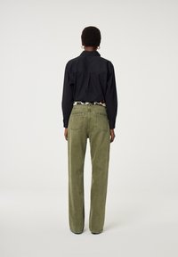 Zwarte collared shirt gecombineerd met hooggewaide, wijdvallende olijfgroene broeken, voorzien van een patroonriem en details op de achterzak.