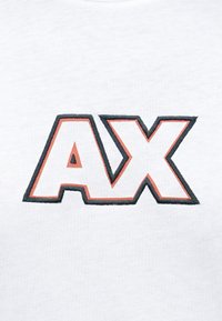 Bjela tkanina s izvezenim slovima "AX" obrubljenim crnom i crvenom koncem.
