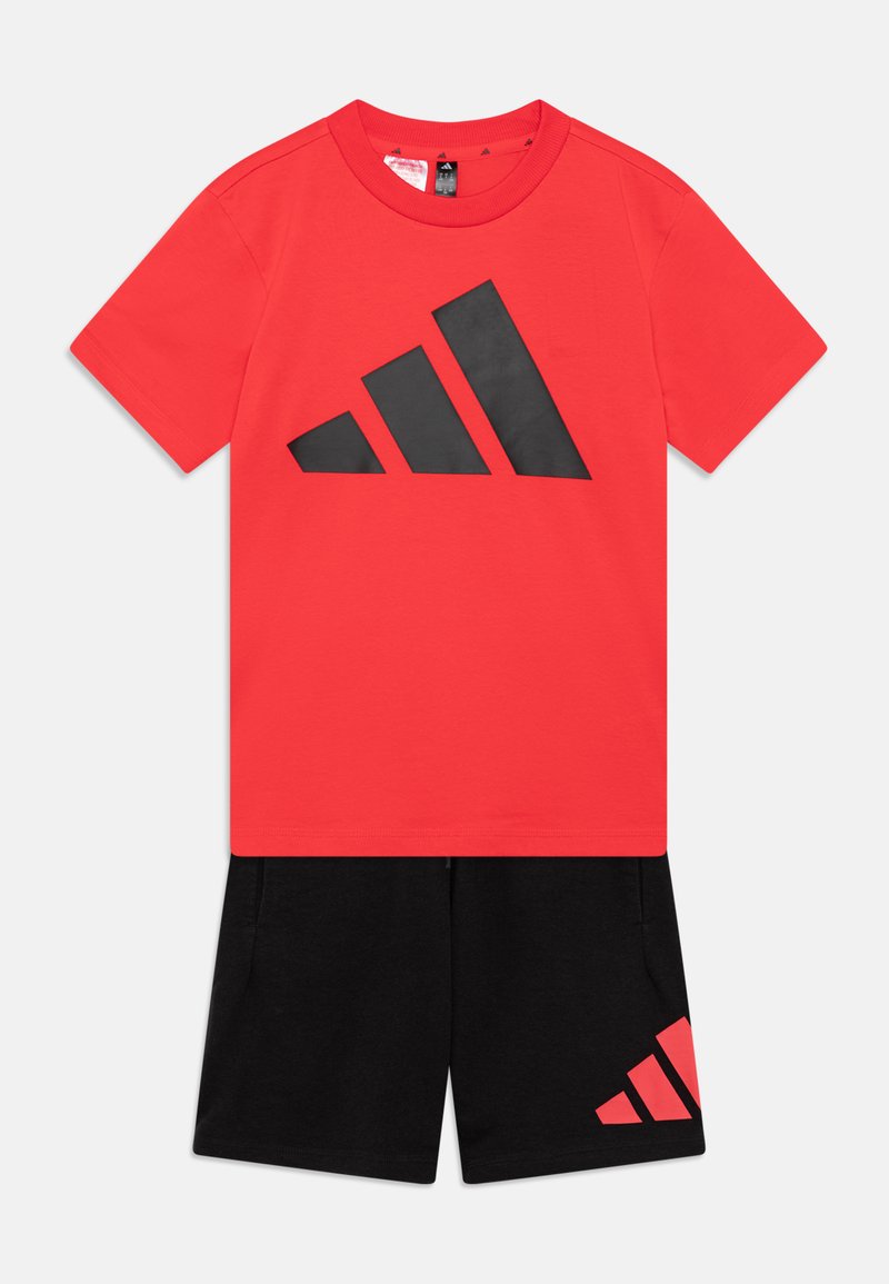 Camiseta roja con un gran logo negro de Adidas; pantalones cortos negros con un logo rojo de Adidas más pequeño, ambos hechos de suave tela de algodón.