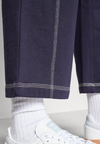 Marineblauwe cropped broek met witte stiksels, in combinatie met textuur witte sokken en witte Adidas sneakers met een lichtblauw logo.