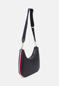 Marineblaues Schultertasche aus glattem Material, mit einer geschwungenen Silhouette, goldenen Beschlägen und rot-weißen gestreiften Akzenten an der Seite.