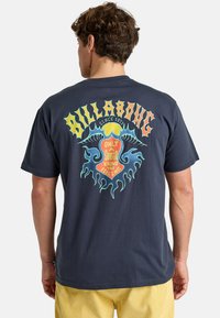 Tricou din bumbac închis la culoare, având un grafic colorat în stil retro pe spate, cu text și elemente de valuri. Mâneci scurte și croială lejeră.