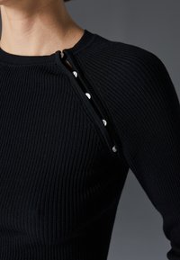 Black ribbed knit top featuring a round neckline and a side closure with silver-tone buttons. Close-up view highlighting texture and detailing.