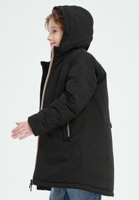 Doudoune noire à capuche avec fermeture éclair frontale ornée d'un accent doré, poches latérales et un design épuré pour la chaleur.