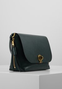 Borsa in pelle verde con chiusura a pattina, hardware dorato e zip laterale. Presenta una texture liscia e un design strutturato.