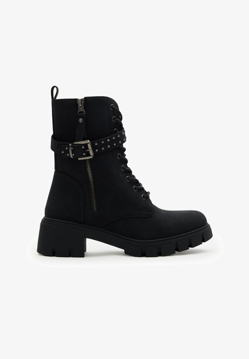 Botín negro hasta el tobillo con tacón grueso, cremallera lateral, parte delantera con cordones y detalle de correa con hebilla con tachuelas sobre fondo blanco.
