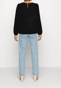Maglietta nera a maniche lunghe con dettaglio a chiave sul retro, abbinata a jeans alta vita di colore azzurro chiaro. La maglietta presenta maniche a sbuffo.