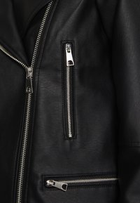 Czarna skórzana kurtka z srebrnymi suwakami, teksturowaną powierzchnią i dwiema zasuwanymi kieszeniami, jedną ukośną i jedną poziomą.